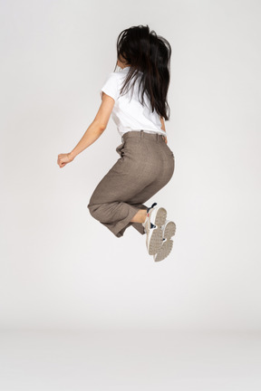 Три четверти сзади прыгающей молодой леди в бриджах и футболке, сгибающей колени