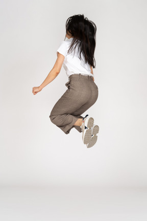 Three-quarter back view of a jumping young lady in breeches and t-shirt bending knees