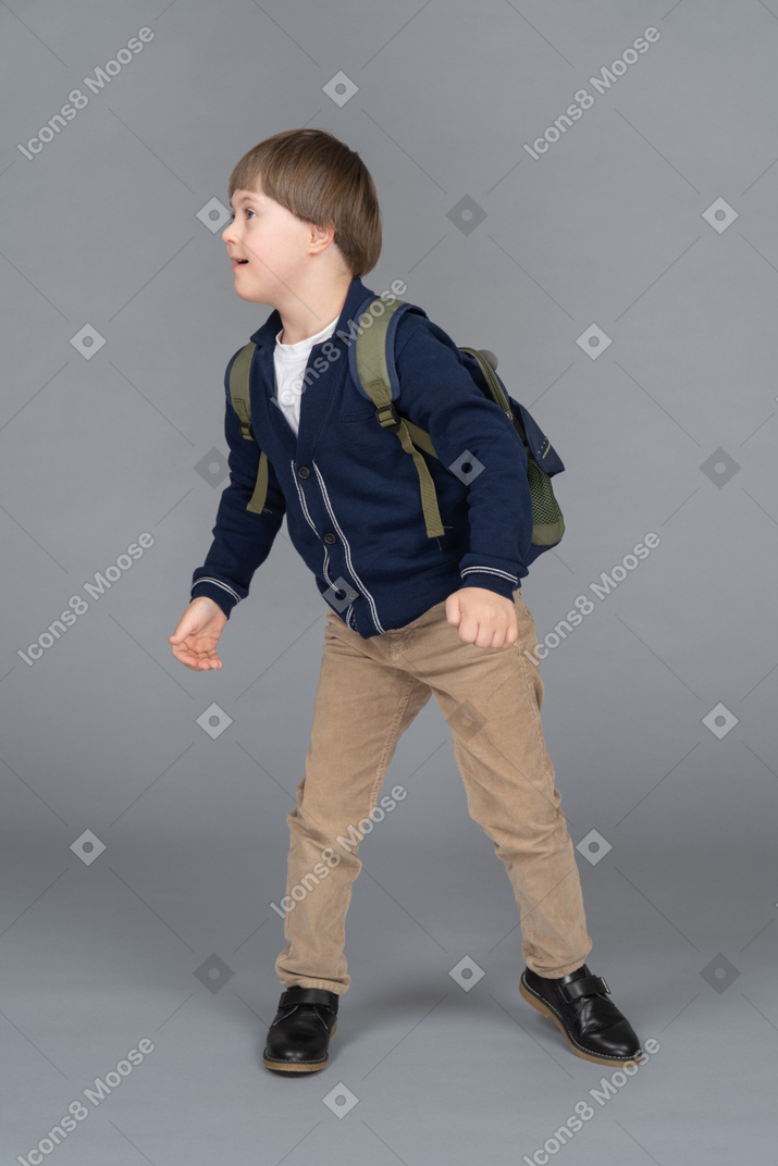 Kleiner junge mit rucksack, der sich zur seite dreht