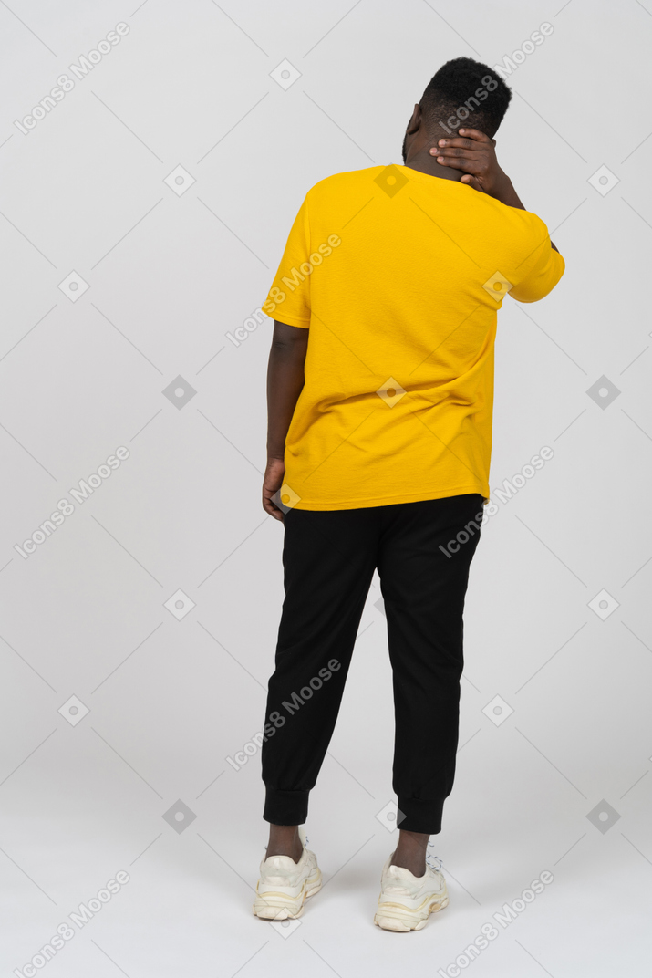 Vista de trás de um homem de pele escura em uma camiseta amarela tocando seu pescoço