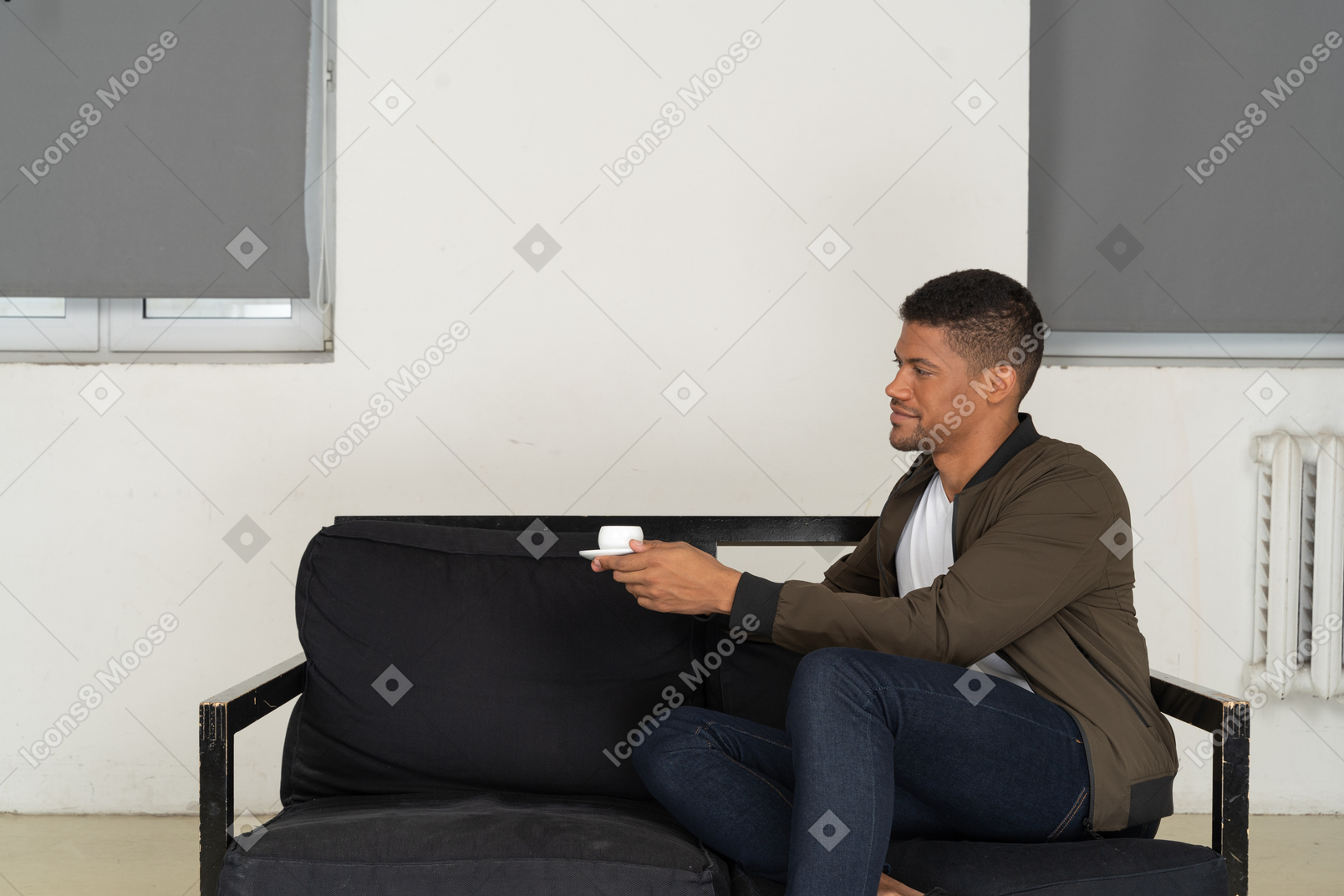 Вид в три четверти молодого человека, мечтающего, сидящего на диване с чашкой кофе