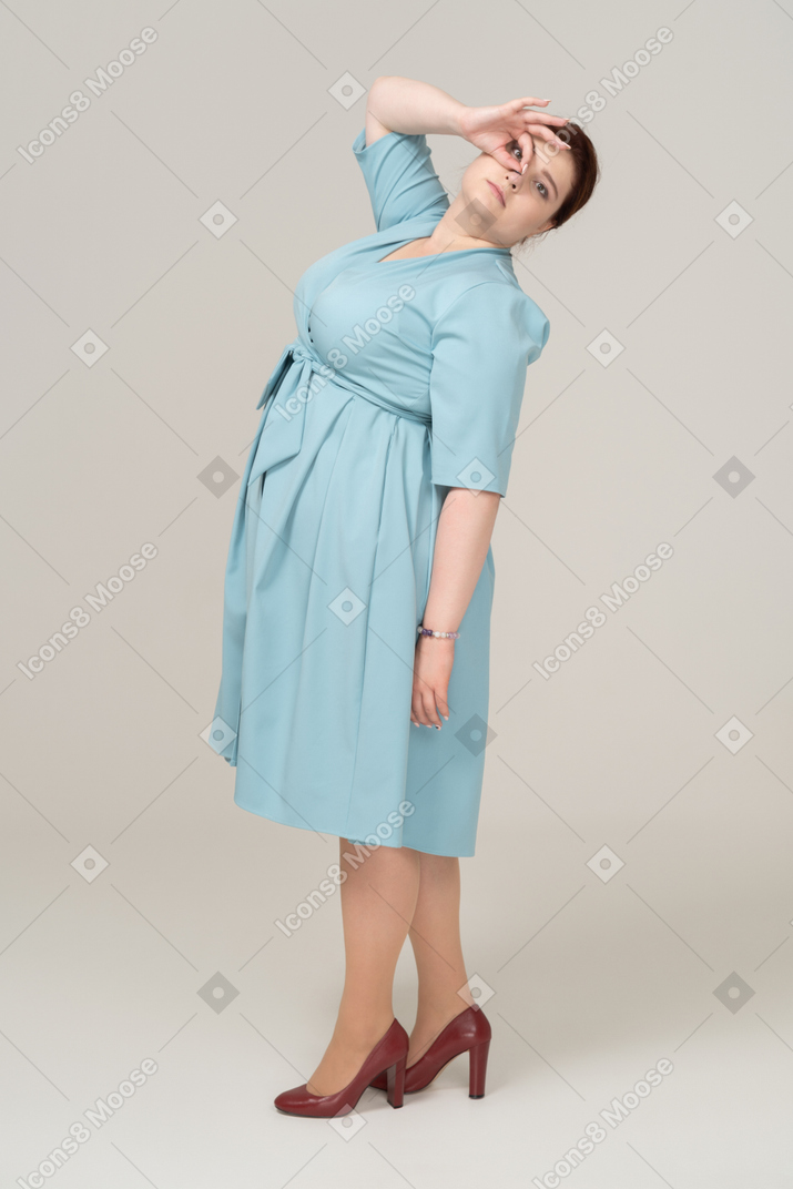 Вид сбоку на женщину в синем платье, смотрящую сквозь пальцы