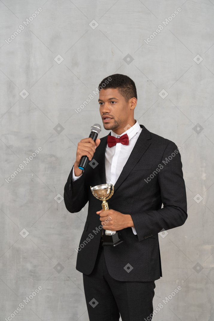 Man in a tuxedo holding microphone and trophy