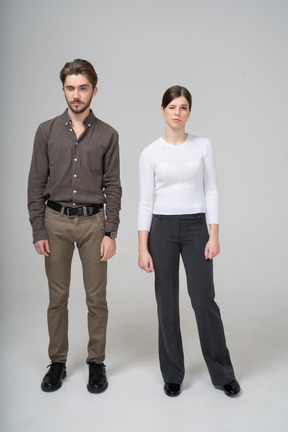 眨眼的年轻夫妇，在办公室服装站着不动的前视图