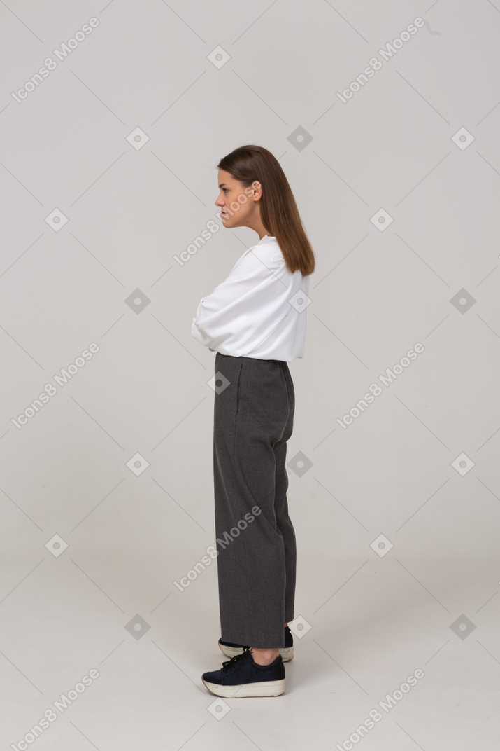 Vista lateral de una joven enojada en ropa de oficina cruzando los brazos