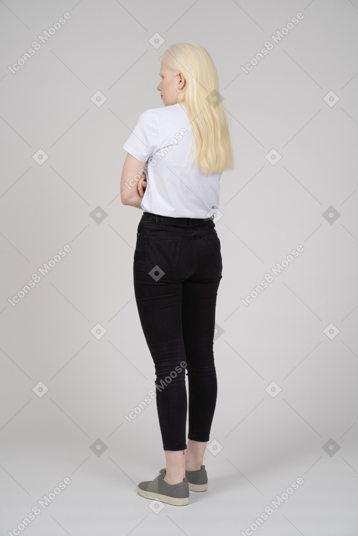 Vista posteriore di tre quarti di una giovane donna in piedi con le braccia incrociate