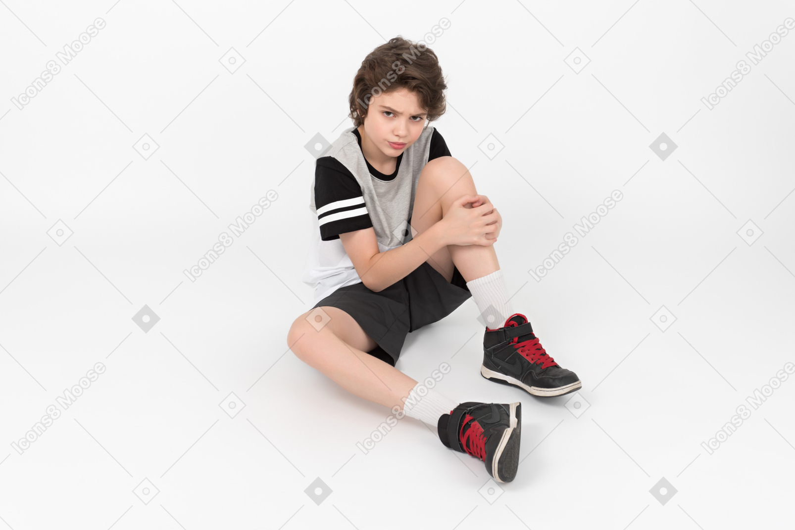 심술 궂은 운동 소년이 바닥에 앉아 다리를 만지고 있습니다.