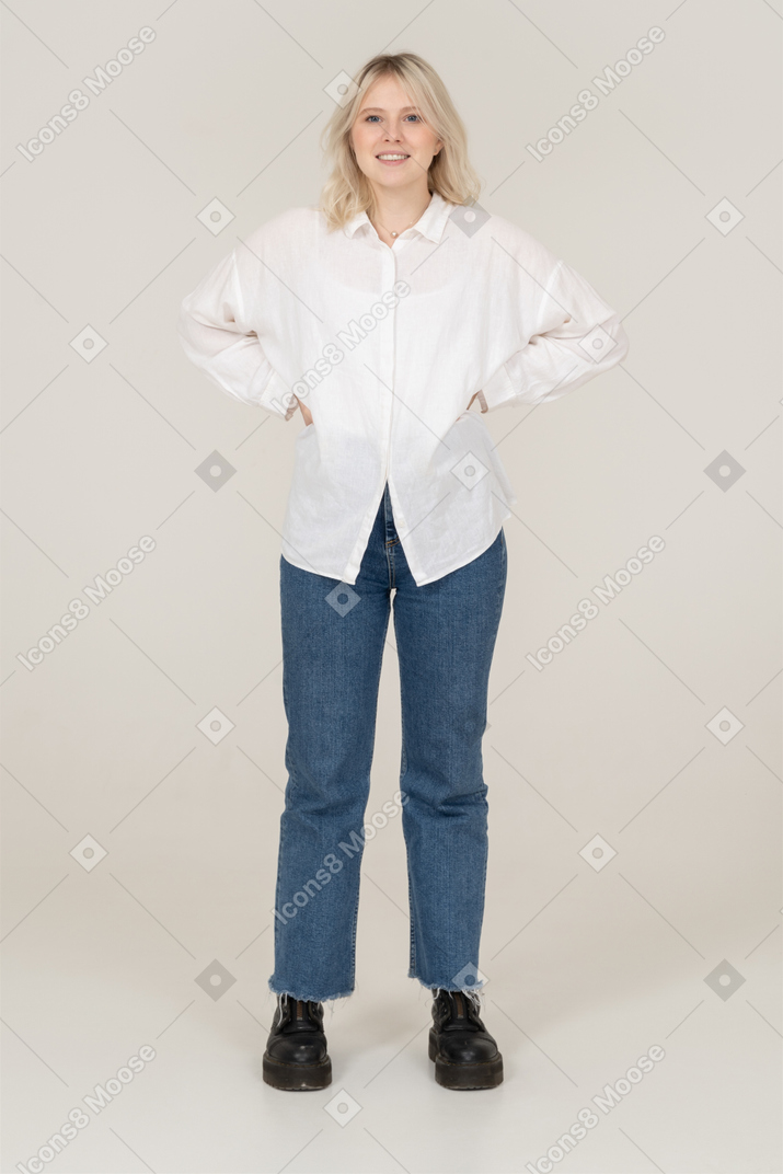 Vista frontal de una mujer rubia en ropa casual poniendo las manos en las caderas y mirando a la cámara