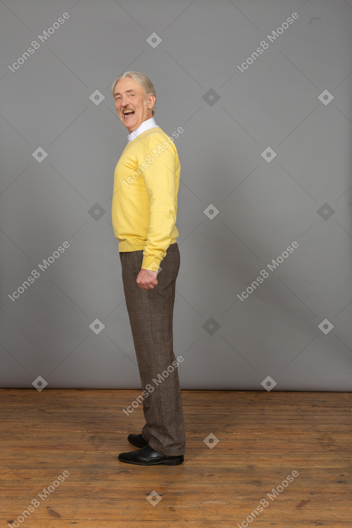 一个微笑的人，在一件黄色的套衫，他的嘴张开看着相机的侧视图