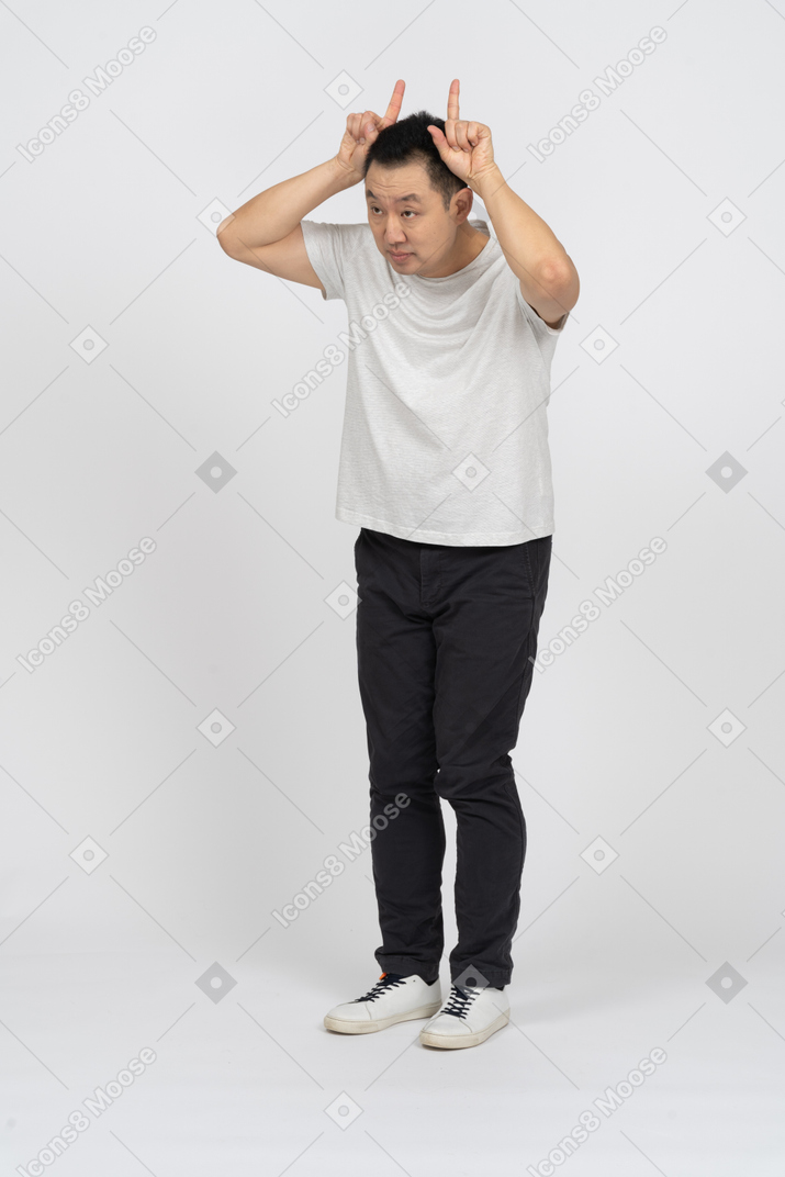Vista frontal de un hombre con ropa informal haciendo cuernos con los dedos