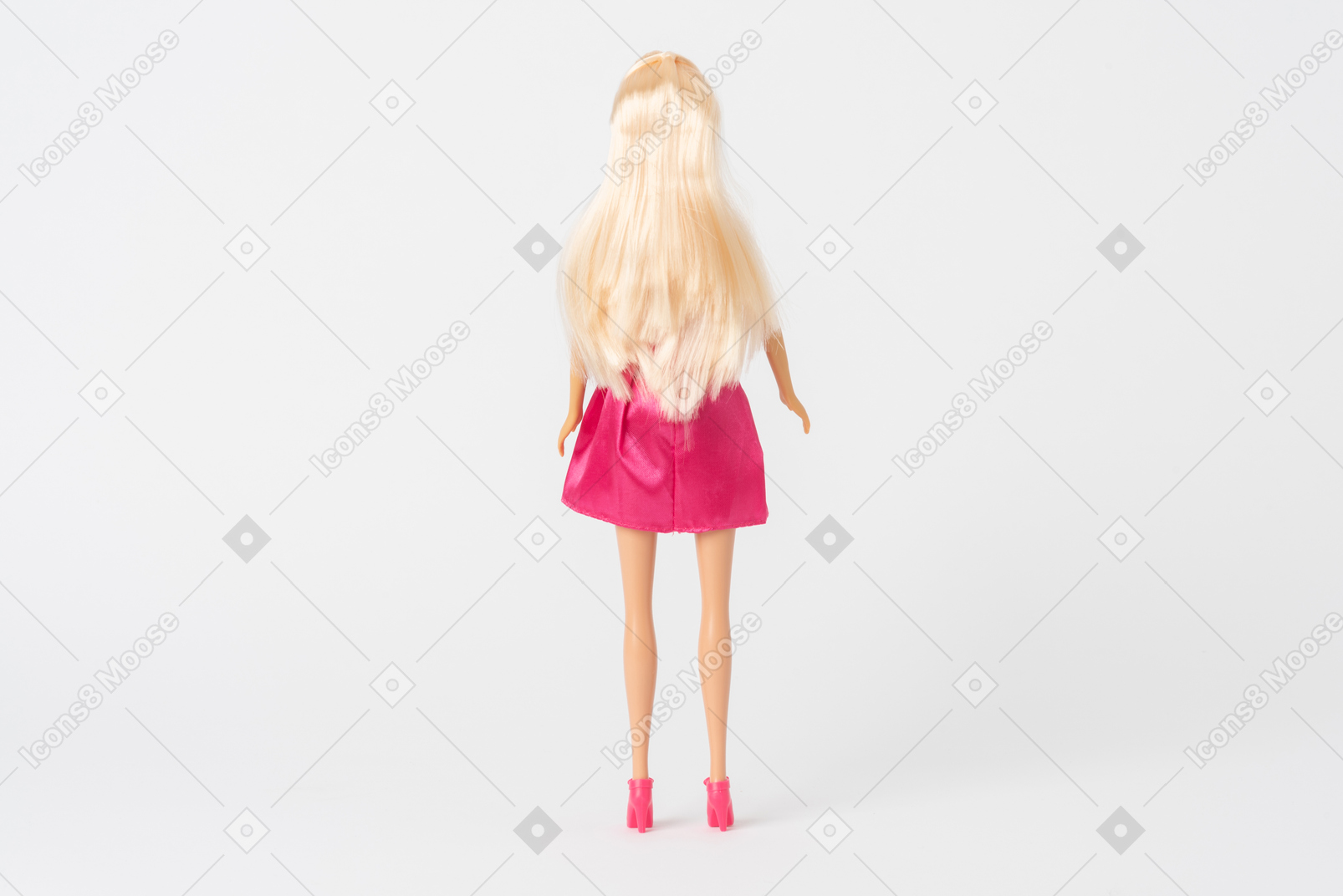 A back shot of a barbie doll in a shiny pink dress and pink high heels standing isolated against a plain white background