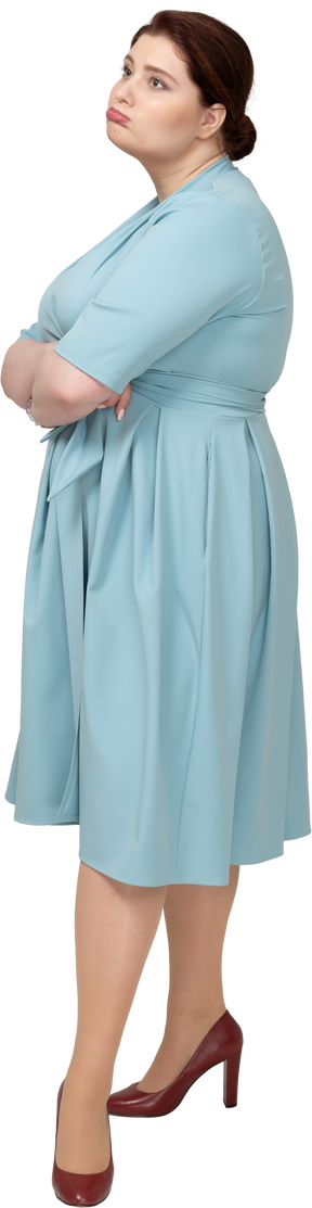 Вид сбоку на женщину в синем платье, стоящую со скрещенными руками