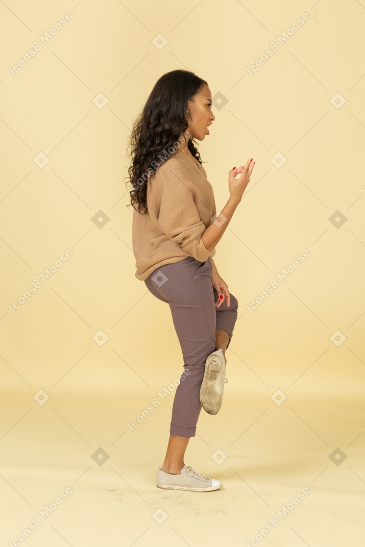 Vista lateral de uma jovem mulher de pele escura aos gritos mostrando um gesto de pedra