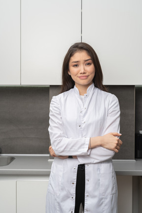 Vue de face d'une femme médecin perplexe regardant la caméra et se croisant les mains