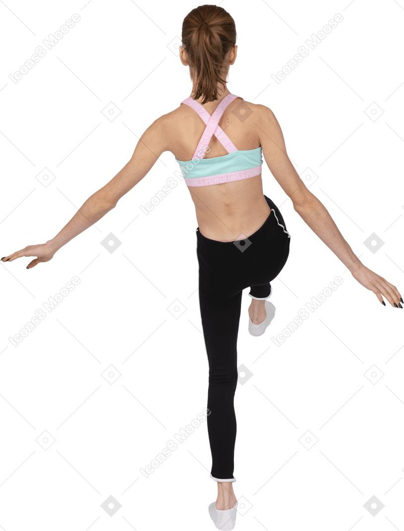 Вид сзади девушки в спортивной одежде, протягивающей руки и поднимающей ногу