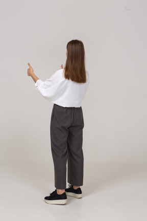 Vista traseira de três quartos de uma jovem com roupa de escritório mostrando os polegares