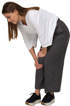 Three-quarter view of a young lady in office clothing bending down & touching knee