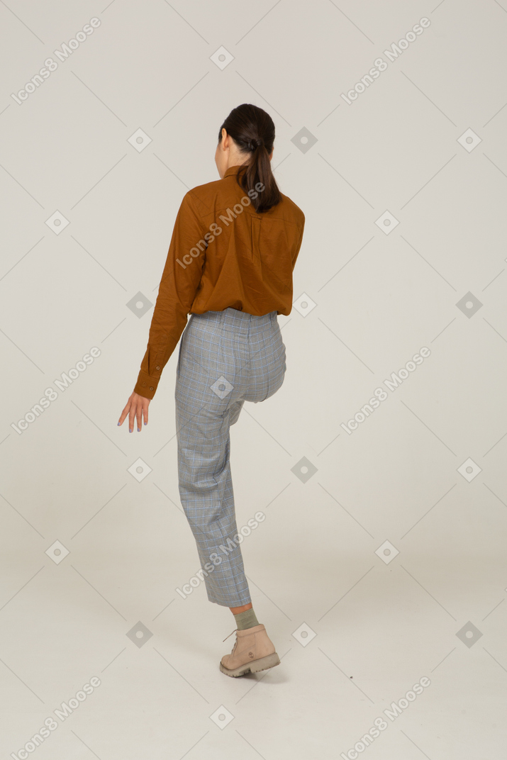 Three-quarter back view of a young asian female in breeches and blouse raising leg