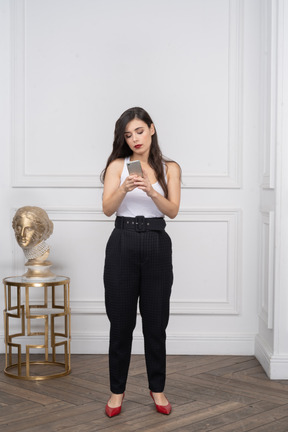 Front view of a young female looking at her phone near golden greek sculpture