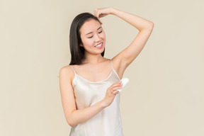 Pretty asian woman applying deodorant on armpit's area