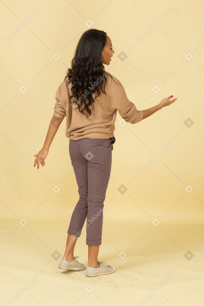 Вид сзади в трех четвертях темнокожей молодой женщины, протягивающей руку