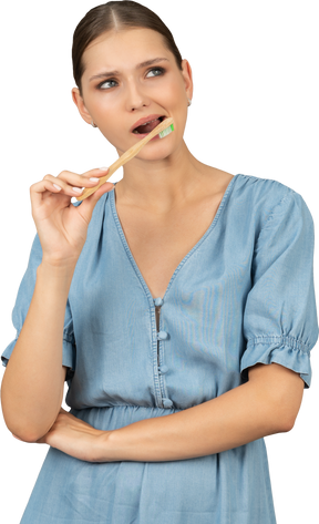 Vista frontal de uma jovem de vestido azul escovando os dentes