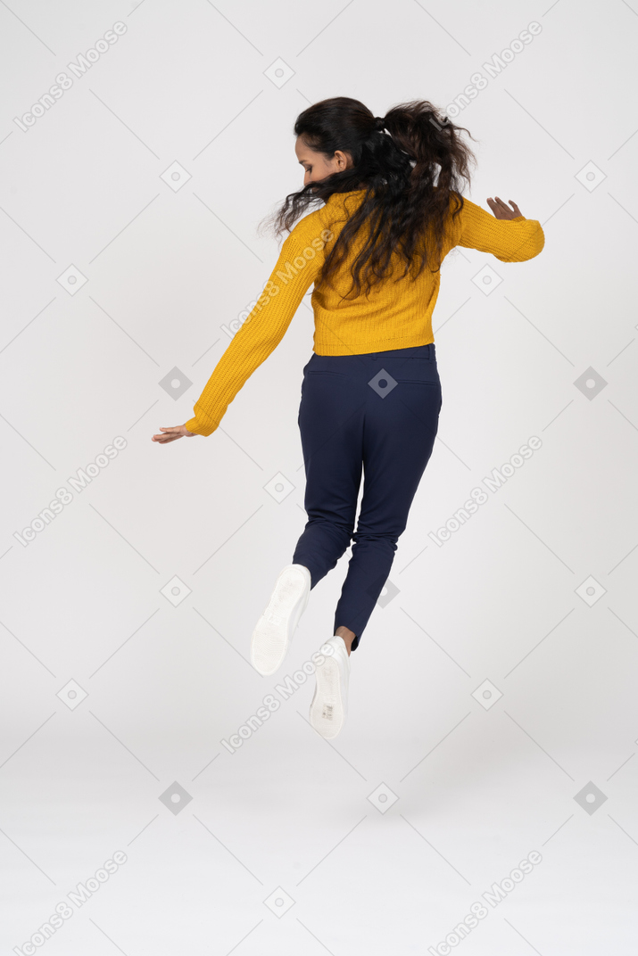 一个穿着休闲服的女孩跳跃并试图触摸她的脚的后视图