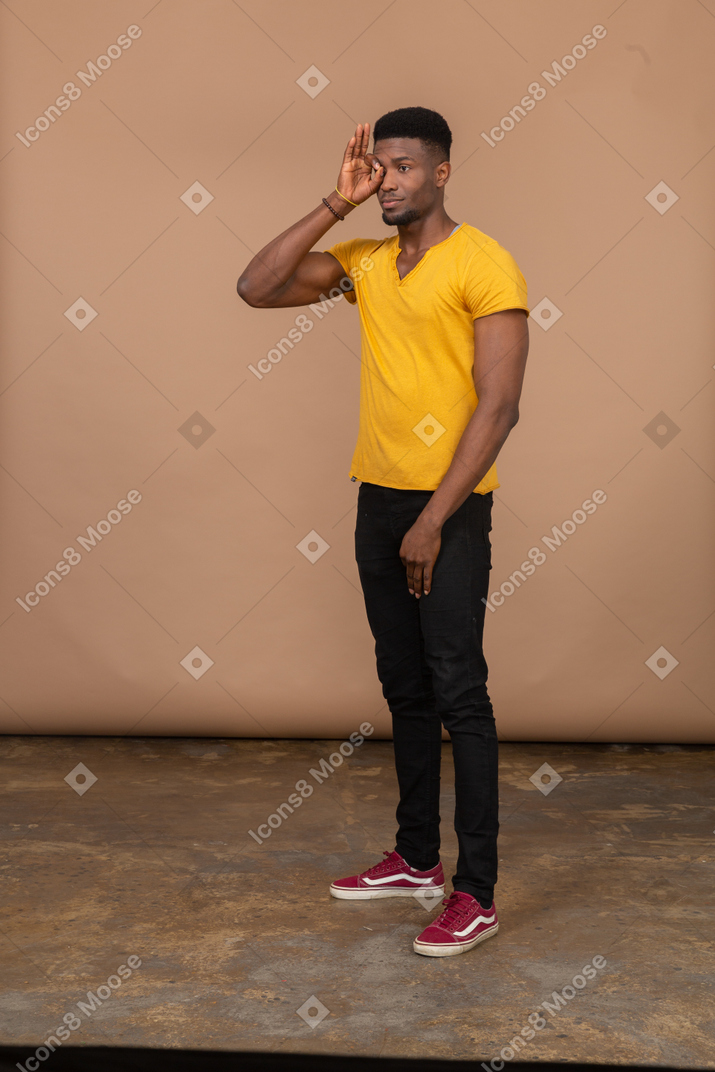 Man in yellow shirt and black pants looking through ok gesture