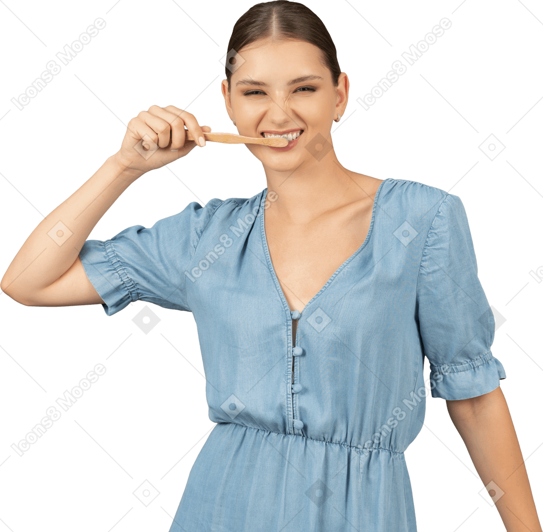 Вид спереди молодой женщины в синем платье, чистящей зубы