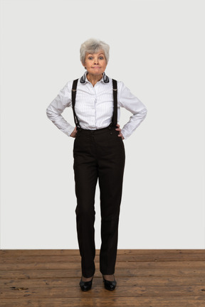 Front view of an old naughty female in office clothes bending down and grimacing putting hands on hips