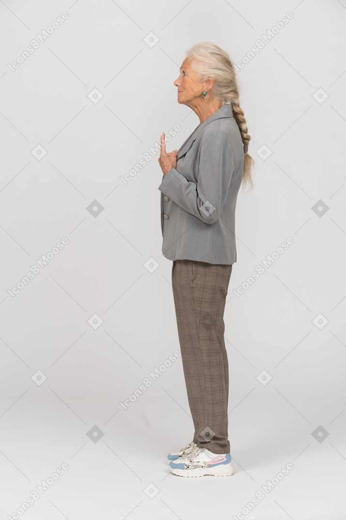 Vista lateral de uma senhora com uma jaqueta cinza apontando para cima com um dedo
