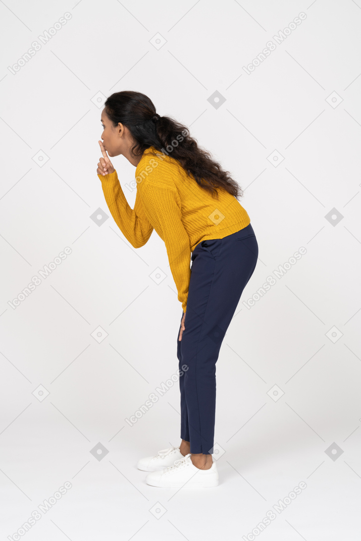 Vista lateral de uma garota com roupas casuais fazendo um gesto de shh