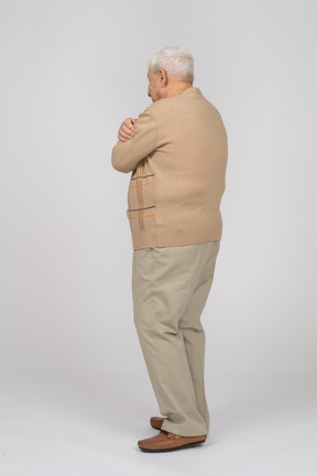 Side view of an old man in casual clothes hugging himself