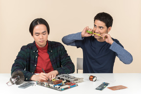 Two young geeks sitting at the table and fixing some details