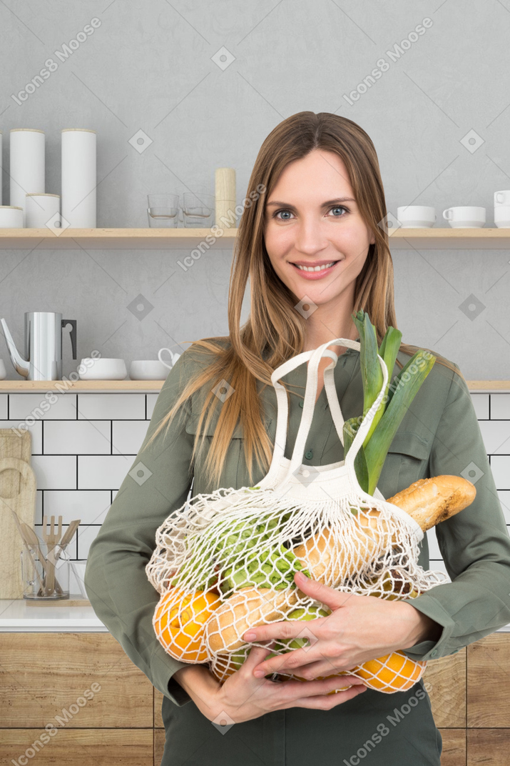 A woman holding a bag full of vegetables in front of a kitchen