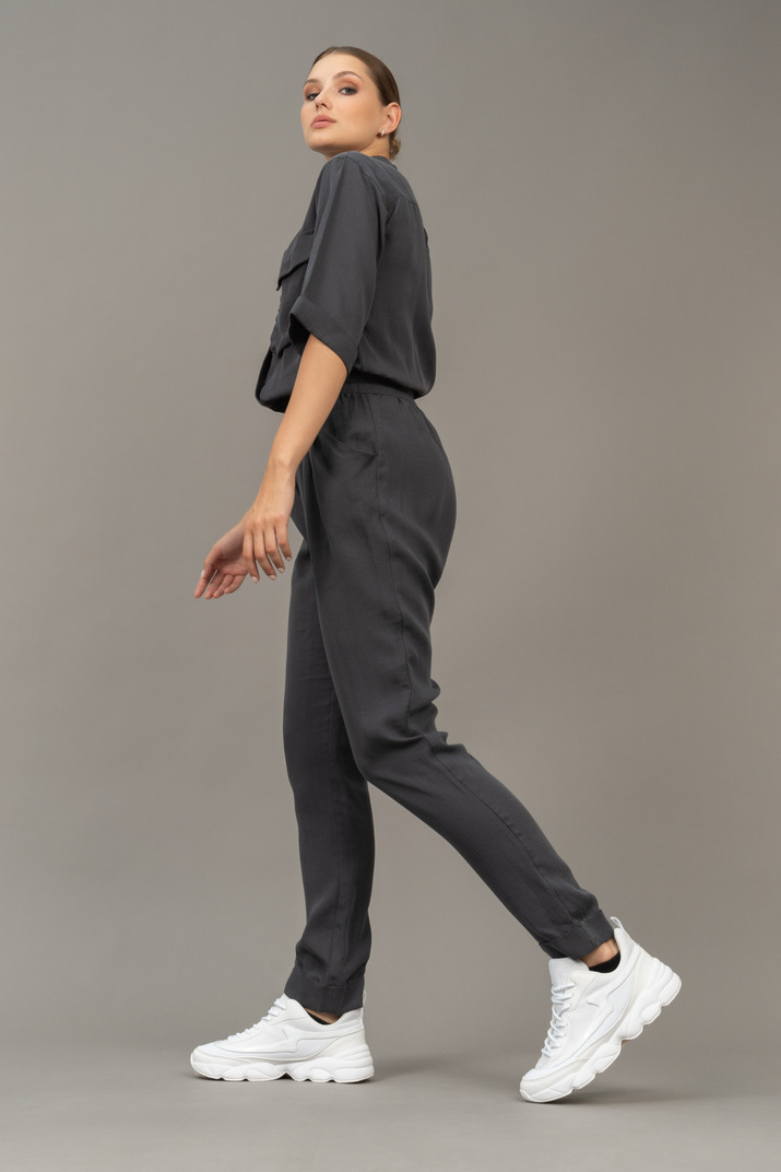 Side view of a walking young woman in a jumpsuit looking at camera