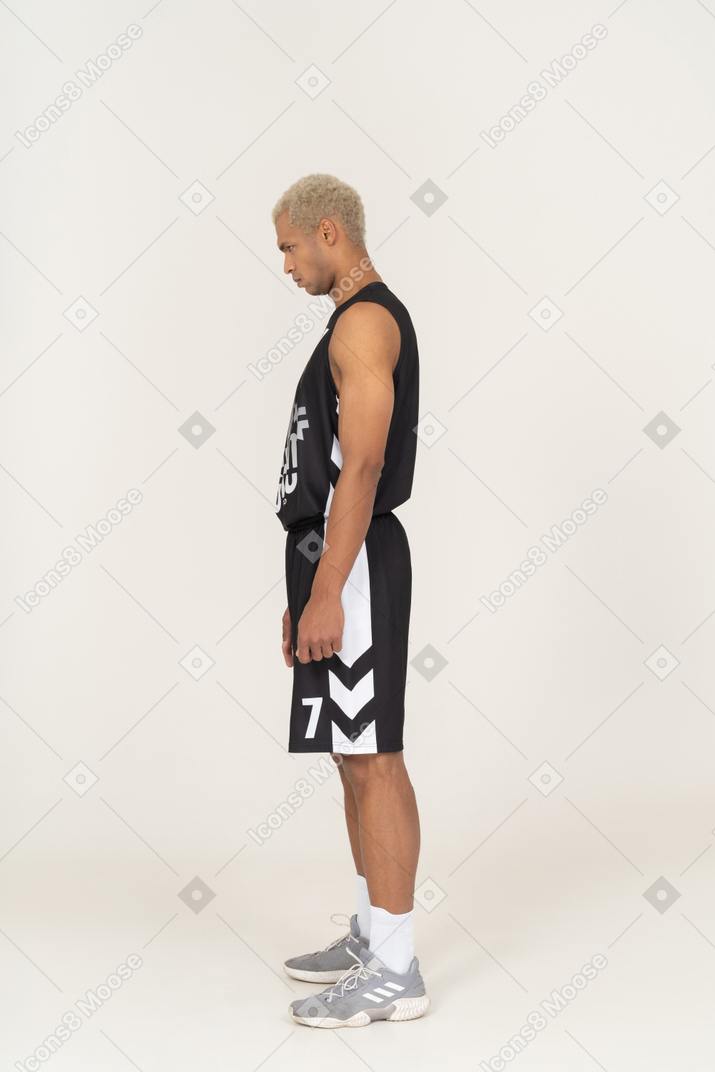Vista laterale di un giovane giocatore di basket maschile in piedi con la testa in giù