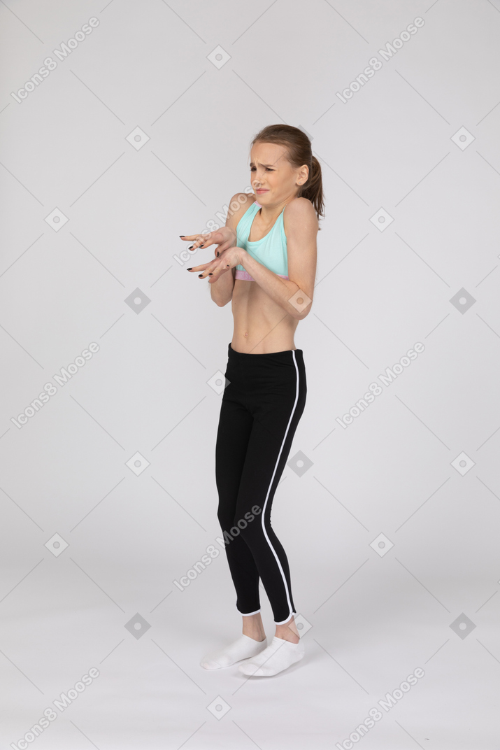 Three-quarter view of a displeased teen girl in sportswear narrowing eyes and gesticulating
