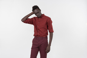 Un joven negro con una camisa roja con mangas enrolladas y pantalones rojo oscuro de pie solo sobre el fondo blanco.