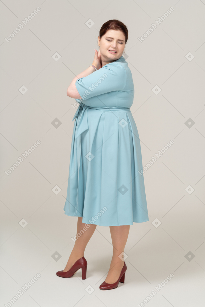 Вид сбоку на женщину в синем платье, страдающую от боли в шее