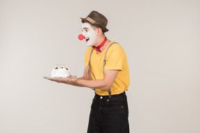 Male clown standing half sideways and holding a cake