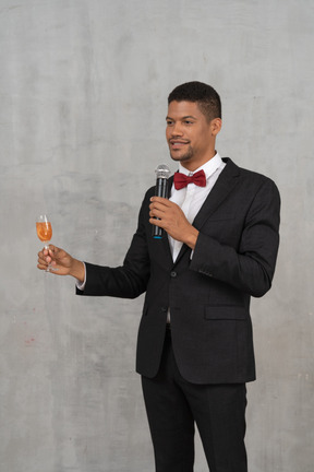 Man in suit holding a glass and talking into a microphone