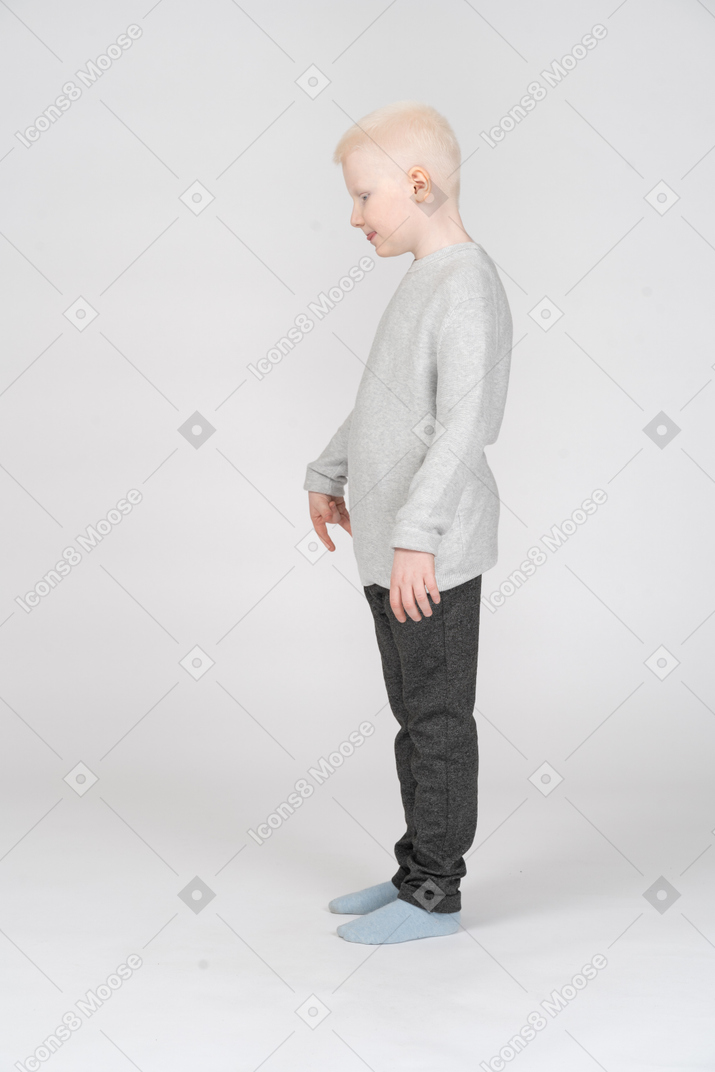 Side view of a gesticulating kid boy showing tongue and pointing down