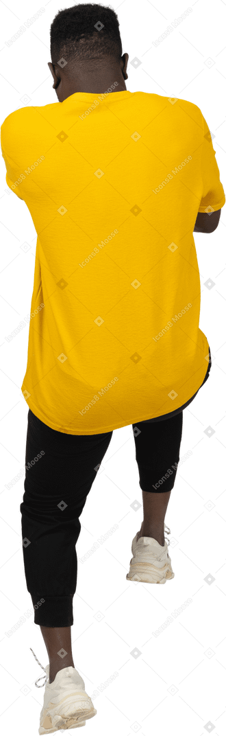 Vista traseira de um jovem de pele escura em uma camiseta amarela pulando para trás
