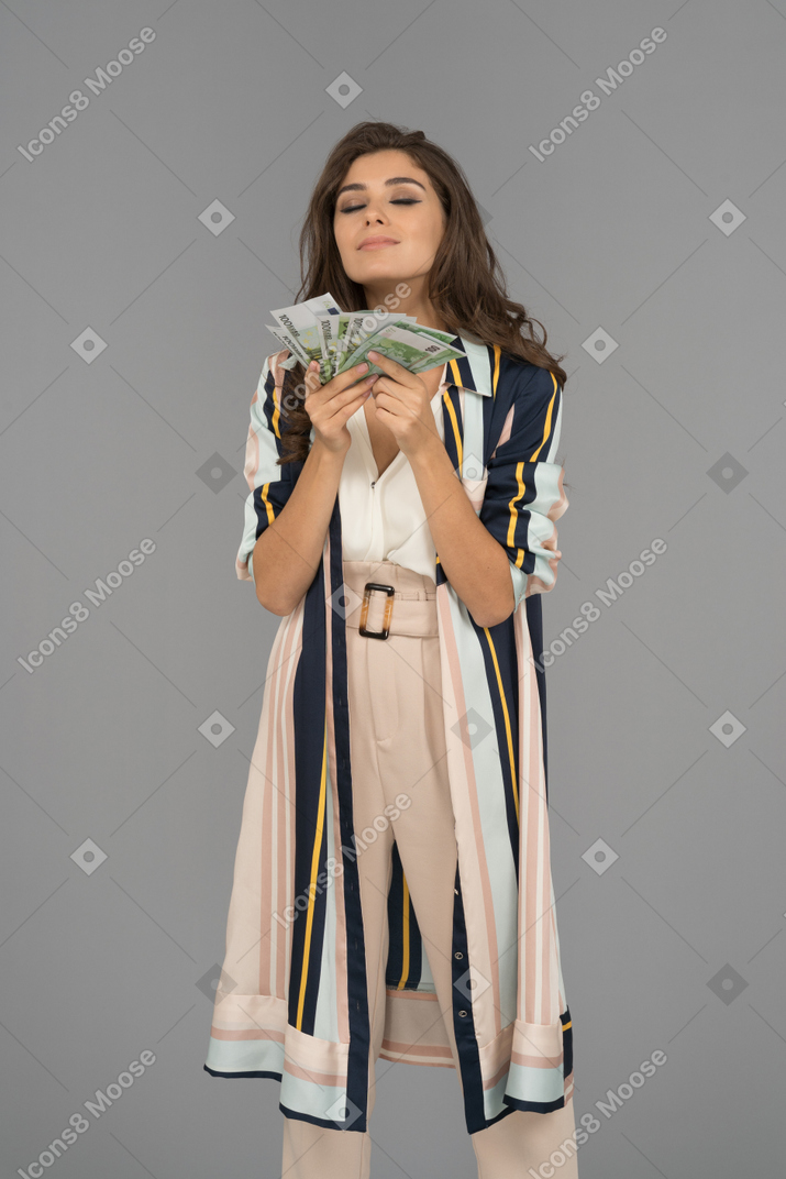 Portrait of a rich young woman enjoying the smell of banknotes