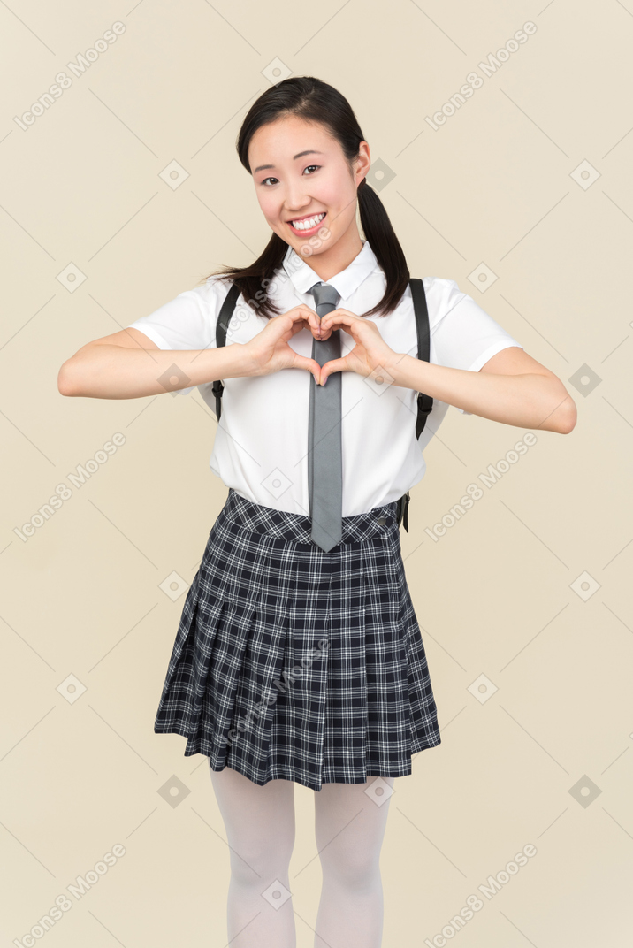 Alegre colegiala asiática mostrando gesto de corazón con ambas manos