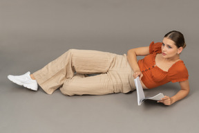 Young woman lies with book while looking away