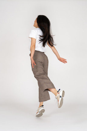 Vista posterior de tres cuartos de una señorita saltando en calzones y camiseta