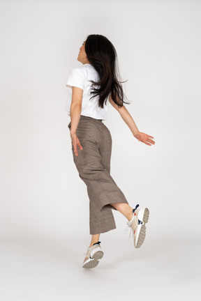 Three-quarter back view of a jumping young lady in breeches and t-shirt