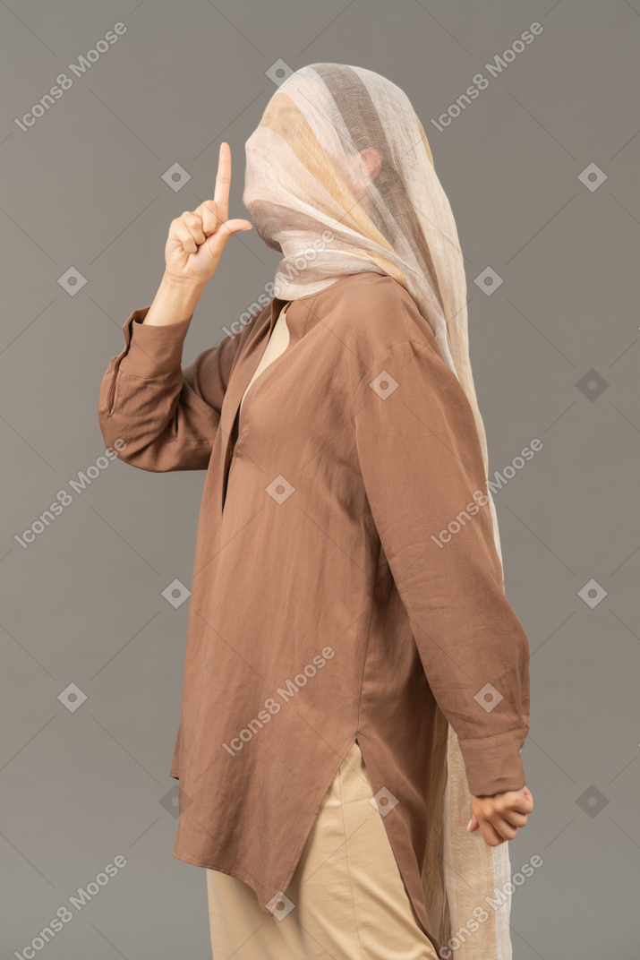Side view of young woman covered with shawl showing shush gesture